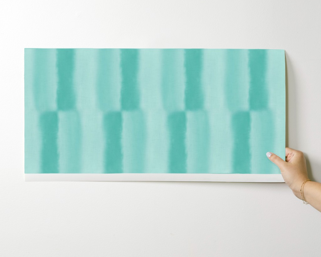 Hand holding a teal abstract striped painting against a white background